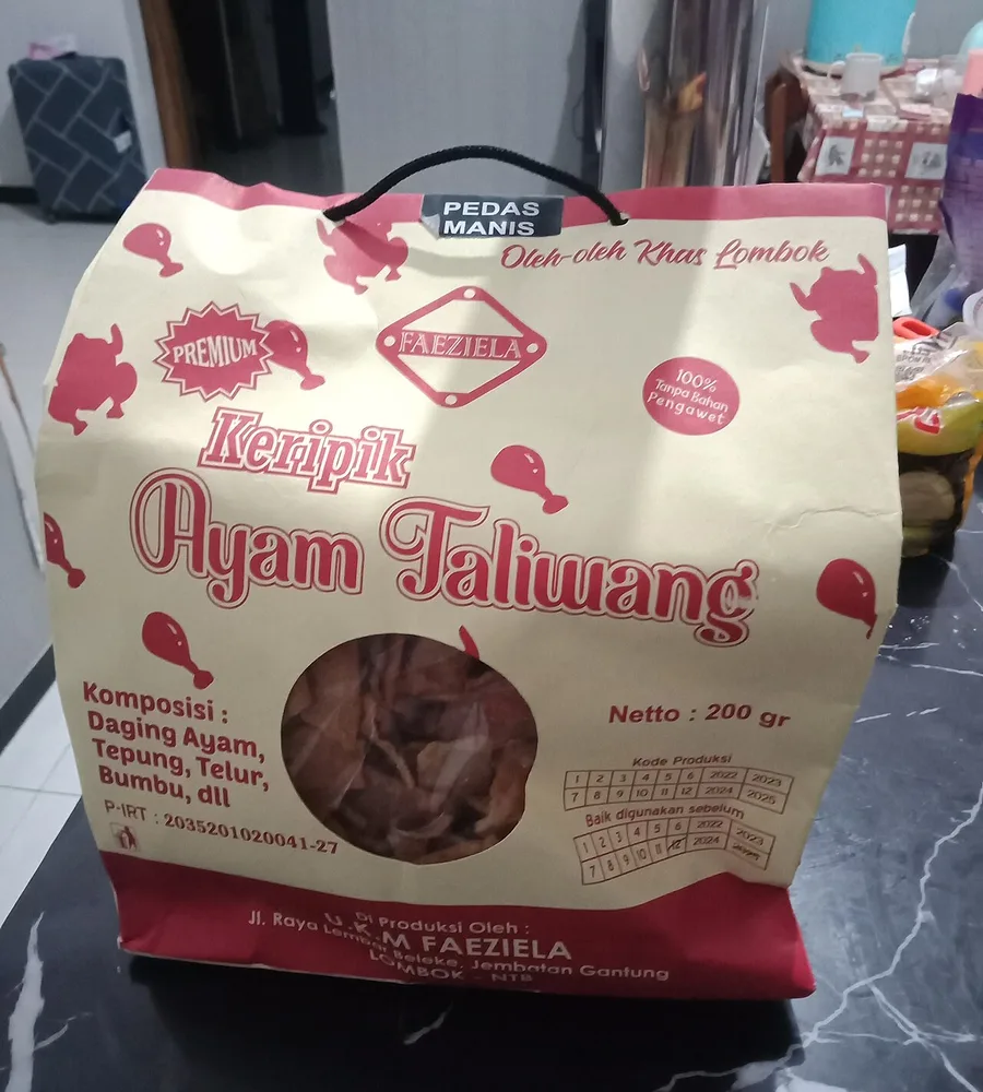 Kemasan Keripik Ayam Taliwang merek Faeziela, oleh-oleh khas Lombok, berupa kantong krem bergambar paha ayam merah dengan jendela transparan dan tali jinjing hitam