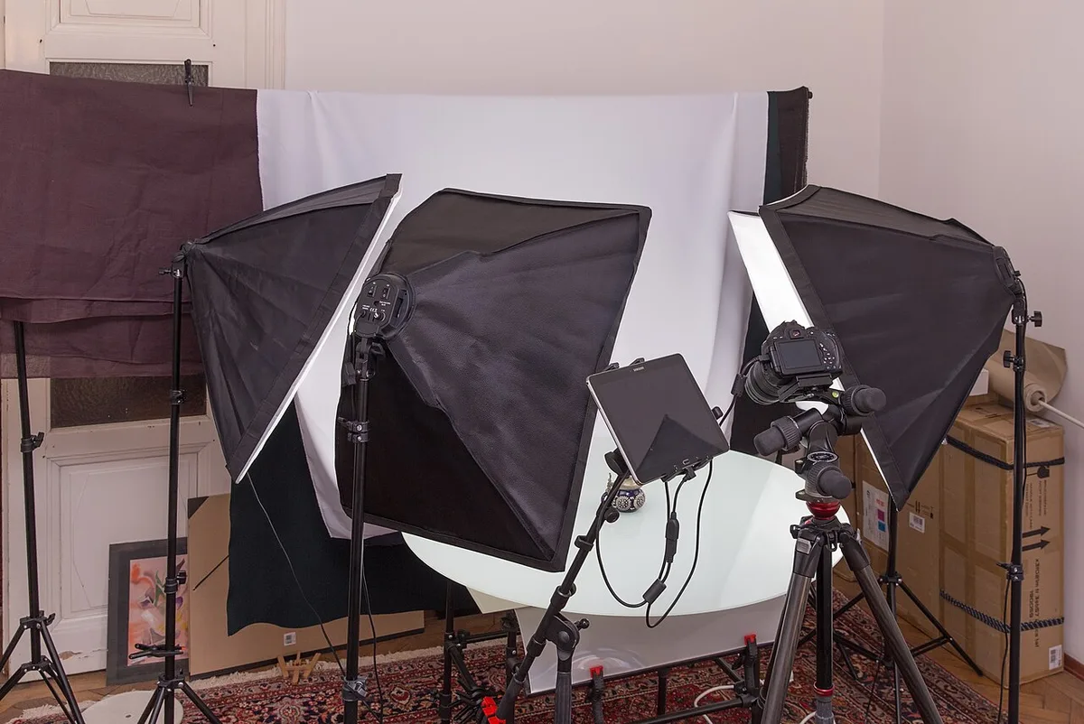 Studio foto produk dengan tiga softbox, backdrop putih melengkung, kamera di atas tripod, dan tablet sebagai monitor